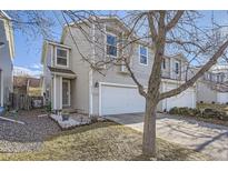 Two-story home featuring a white garage door, tan siding, manicured lawn, and a small garden area in front at 22150 E Berry Pl, Aurora, CO 80015