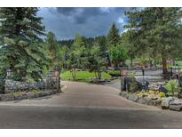 Stately brick driveway leads to a secure gated entrance surrounded by lush landscaping and mature trees at 97 Soda Creek Rd, Evergreen, CO 80439