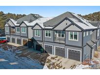 Gray townhouses with attached garages, snow on the roofs, and mountain views in the background at 31191 Black Eagle Dr # 102, Evergreen, CO 80439
