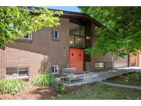 Charming brick home with a vibrant orange front door and inviting bench seating near manicured garden at 6705 E Jewell Ave, Denver, CO 80224