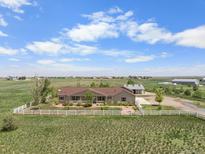 Sprawling ranch-style home with white fence on a lush, open lot and a detached garage on a sunny day at 32501 E 137Th Way, Brighton, CO 80603