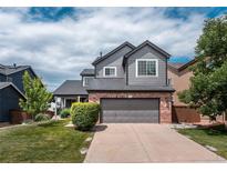 Charming two-story home featuring gray siding, brick accents, a well-manicured lawn, and an attached two-car garage at 9758 Red Oakes Dr, Highlands Ranch, CO 80126