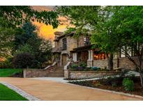 Stately stone home with meticulous landscaping, a winding driveway, and a sunset sky at 45 Charlou Cir, Cherry Hills Village, CO 80111