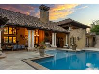 Outdoor pool with stone patio, covered veranda with dining set and grill, all under a stunning sunset sky at 45 Charlou Cir, Cherry Hills Village, CO 80111