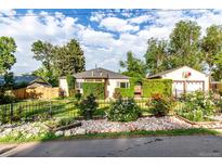 Charming home featuring lush landscaping, a manicured lawn and a wrought iron fence with flower beds at 1060 S Eaton St, Lakewood, CO 80226