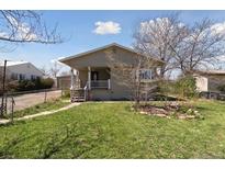 Charming single-story home with a front porch, green lawn, and a chain-link fence at 575 2Nd St, Bennett, CO 80102