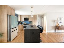 A modern kitchen featuring wood cabinets, stainless appliances, blue backsplash, and a large island with barstool seating at 815 S Jersey St, Denver, CO 80224