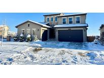 Two-story home with stone accents and a three-car garage in snowy setting at 15454 W Auburn Ave, Lakewood, CO 80228