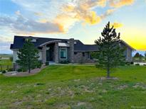 Inviting front exterior with a manicured lawn, stone accents, and beautiful sunset views at 3125 Red Kit Rd, Franktown, CO 80116