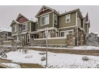 View of townhome exterior with a green facade and stone accents, surrounded by snow-covered landscaping at 23545 E Platte Dr # C, Aurora, CO 80016