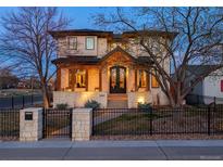 Elegant two-story home boasts stone accents, a covered front porch with wooden columns, and a beautifully landscaped yard with iron fence at 2600 S Adams St, Denver, CO 80210