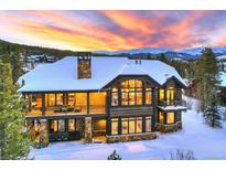 A luxurious, snow-covered home with large windows offers stunning views of the mountain range and fiery sunset at 219 Glen Eagle Loop, Breckenridge, CO 80424
