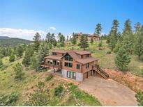 An expansive exterior view showcasing a beautiful cabin-style home nestled among lush greenery and trees at 25704 Shiloh, Conifer, CO 80433
