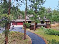 Charming home featuring a large porch, three-car garage, and a winding driveway amid lush trees at 4305 Red Rock Dr, Larkspur, CO 80118