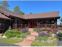 Charming log home featuring a red door, landscaped front yard, a stone walkway, and a cozy front porch at 29095 Summit Ranch Dr, Golden, CO 80401