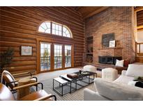 Open living room with log walls, brick fireplace, and access to a private balcony with scenic views at 29095 Summit Ranch Dr, Golden, CO 80401