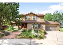 Charming two-story home with brick and siding exterior, lush landscaping, and attached two-car garage on a sunny day at 7603 W Coal Mine Pl, Littleton, CO 80128