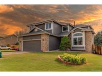 Charming two-story home with manicured front lawn, gray siding, and brick accents at sunset at 4889 S Elkhart Ct, Aurora, CO 80015