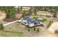 Expansive aerial view showcases a modern farmhouse with lush landscaping and a charming outdoor firepit area at 1567 Arrowpoint Ct, Franktown, CO 80116