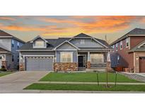 Charming two-story home with stone accents, manicured lawn, and an inviting covered front porch at sunset at 20795 Scenic Park Dr, Parker, CO 80138