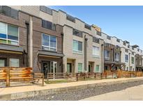 Modern townhomes with mixed brick and siding exteriors, complemented by wooden fences and rooftop decks against a clear blue sky at 3520 W Conejos Pl # 11, Denver, CO 80204