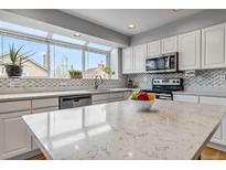 Bright kitchen features white cabinetry, stainless appliances, quartz countertops, and natural light from a large window at 12551 W 84Th Cir, Arvada, CO 80005