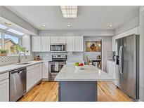 Modern kitchen with stainless steel appliances, white cabinetry, and large island with quartz countertops at 12551 W 84Th Cir, Arvada, CO 80005