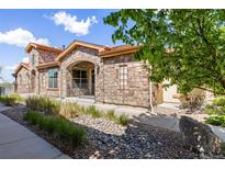 Charming stone townhouse exterior featuring a quaint patio and river rock landscaping under a partly cloudy sky at 2317 Primo Rd # A, Highlands Ranch, CO 80129
