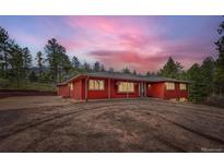 Stunning exterior of red home with inviting front yard and beautiful sunset sky in the background at 4776 Red Rock Dr, Larkspur, CO 80118