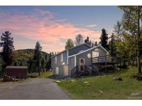 Charming two-story home featuring a deck, lush landscaping, and scenic mountain views at sunset at 32252 Steven Way, Conifer, CO 80433