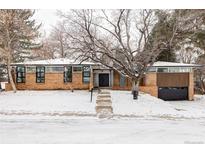 Modern brick home featuring large windows, a flat roof, a two-car garage, and a snowy front yard and mature landscaping at 3611 S Hillcrest Dr, Denver, CO 80237