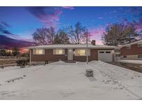 Brick ranch house with attached garage, snow-covered yard, and twilight sky at 12008 W Mexico Pl, Lakewood, CO 80228