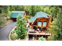 Stunning wooden cabin with expansive deck featuring a hot tub and mountain views surrounded by lush greenery and tall trees at 12191 Tecumseh Trl, Conifer, CO 80433