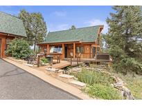 Inviting cabin showcasing a lush landscape, wooden deck with hot tub, and a cozy fire pit area at 12191 Tecumseh Trl, Conifer, CO 80433