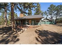 Charming single-story home with a stone chimney and a detached two-car garage nestled among mature trees at 28539 Douglas Park Rd, Evergreen, CO 80439