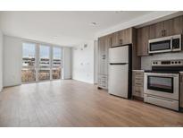 Bright, open-concept living room with modern kitchen featuring stainless steel appliances and wood cabinets at 3575 Chestnut Pl # 702, Denver, CO 80216
