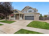 Charming two-story home with brick accents, a gray garage door, well-kept lawn, and a welcoming front porch at 15378 E 99Th Way, Commerce City, CO 80022