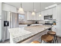 Modern kitchen with stainless steel appliances, white cabinets, and a large speckled granite island with bar stool seating at 8481 Dawson Dr, Denver, CO 80229