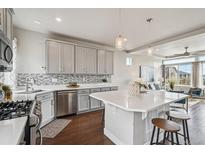Modern kitchen featuring stainless steel appliances, gray cabinetry, a white countertop island with seating, and stylish backsplash at 8095 E 128Th Pl, Thornton, CO 80602
