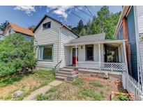 Charming home with a red front door and a cozy porch, nestled amidst lush greenery and a bright sky backdrop at 1324 Virginia St, Idaho Springs, CO 80452
