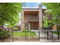 Contemporary multi-story home with stone accents, a balcony, manicured lawn and a black metal fence at 2114 Lowell Blvd, Denver, CO 80211