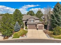 Beautiful two-story home with a three-car garage and manicured front lawn, surrounded by mature trees at 907 Greenridge Ln, Castle Pines, CO 80108