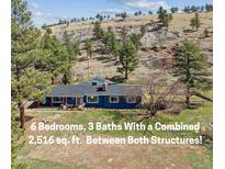 Charming blue ranch home with a covered front porch nestled on a hillside with mature trees at 5384 Olde Stage Rd, Boulder, CO 80302