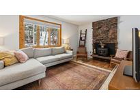 Cozy living room featuring a stone fireplace, comfortable sofa and a view of the trees at 28254 Tresine Dr, Evergreen, CO 80439