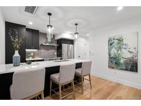 Modern kitchen featuring black cabinets, stainless steel appliances, and a bright white countertop island with chairs at 2451 Lawrence St # 2, Denver, CO 80205