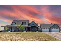 Gray two-story house with a large front porch, three-car garage, and beautiful sunset at 402 S County Road 129, Bennett, CO 80102