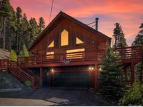 Charming two-story cabin featuring a spacious deck, garage, and picturesque wooded surroundings at sunset at 451 Harris Dr, Idaho Springs, CO 80452