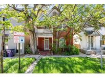 Charming two-story brick home with a cozy front porch and lush green lawn, shaded by mature trees at 2410 W 36Th Ave, Denver, CO 80211
