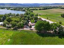 Beautiful aerial view of property with mature trees, white fence, large grassy field, and a lake nearby at 7390 Ute Hwy, Longmont, CO 80503