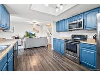 Open kitchen featuring stainless steel appliances, wood floors, and blue cabinets flowing into the living room at 1080 S Yampa St, Aurora, CO 80017